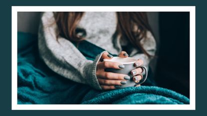 woman on couch in blanket holding a cup of tea