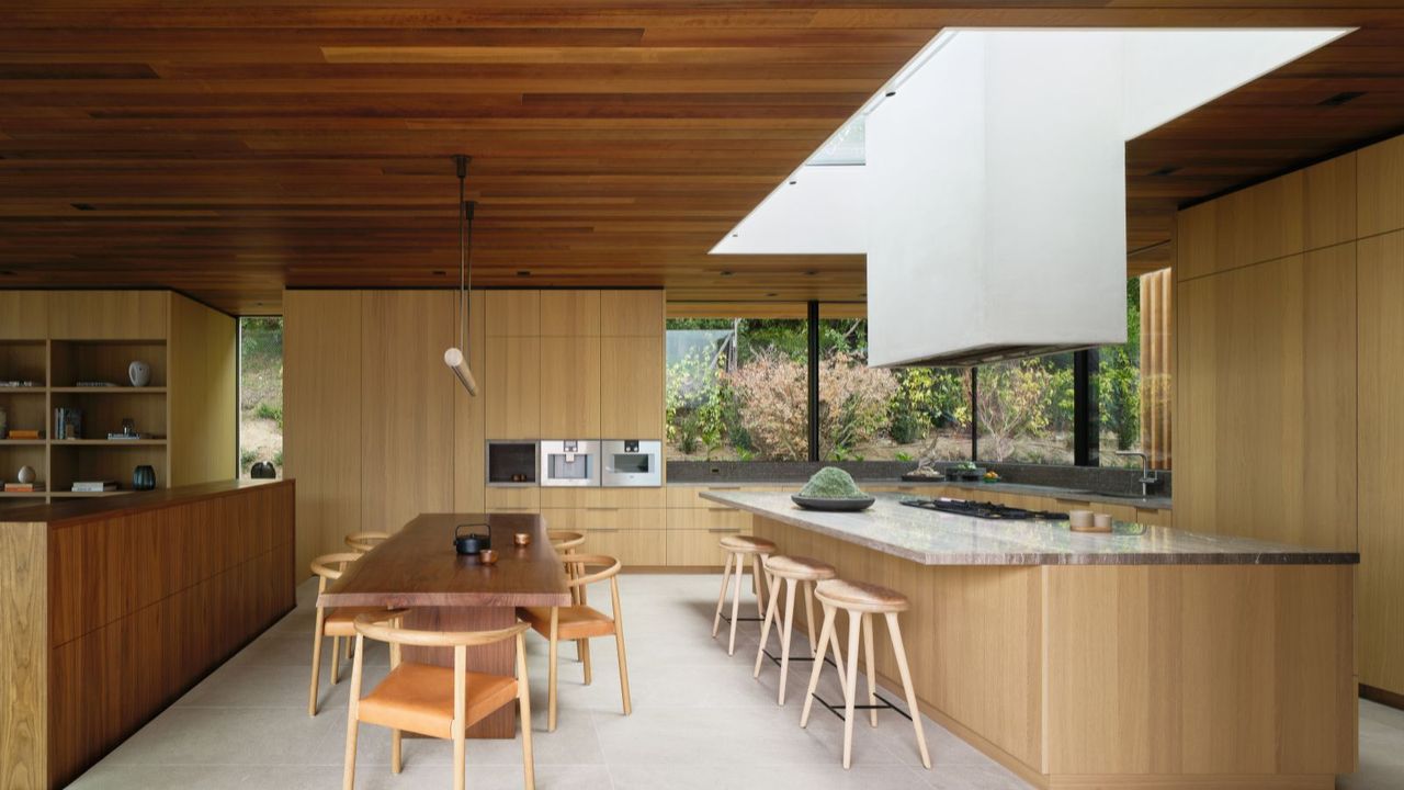 Wood open plan kitchen dining room with large island and wooden chairs and long wood dining table