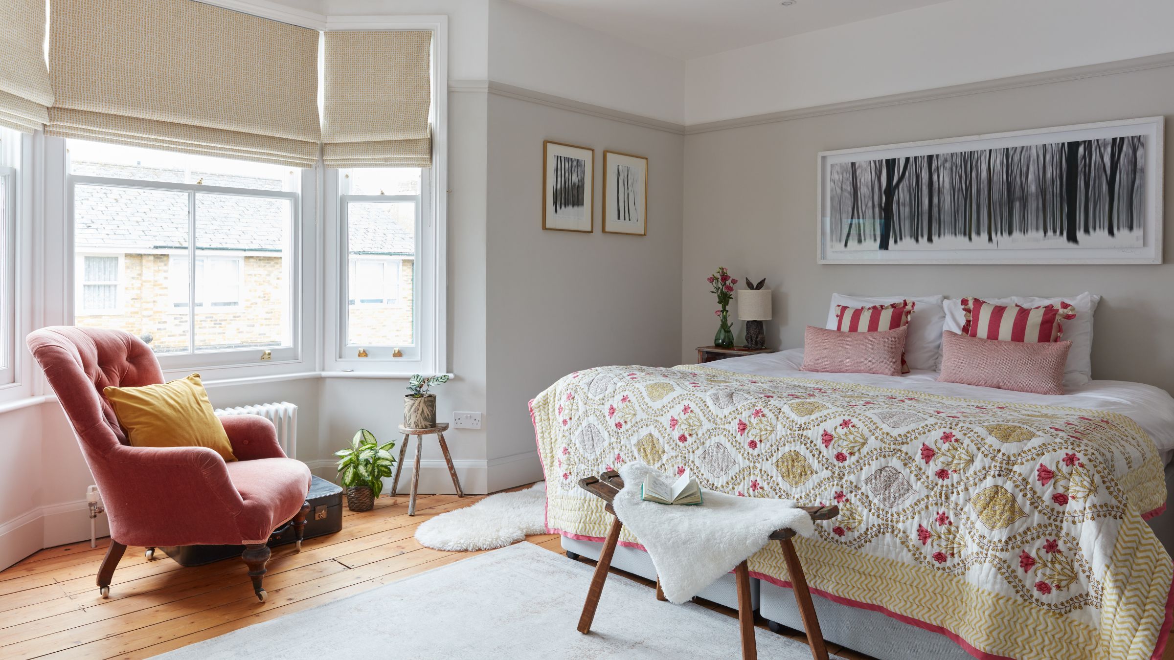 neutral painted period bedroom with bay window and a pink accent chair in front of it, and a large bed on the right hand side