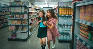 An episodic still from Who Is Erin Carter? showing Erin (Evin Ahmad) with her arms around daughter Harper's (Indica Watson) shoulders. They are both slightly hunched forwards and the shelves around them are out of focus, implying that they are moving quickly