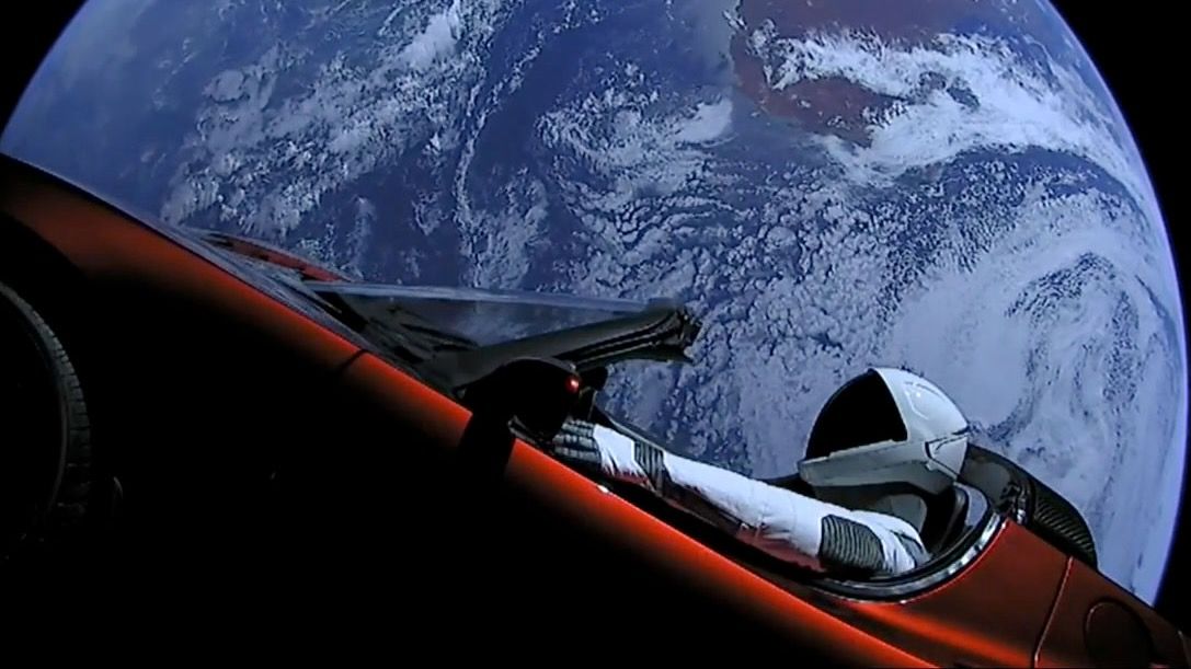 a mannequin in a black and white spacesuit sits in a red convertible in space, with earth in the background