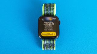 Detail shot of an Apple Watch SE on a bright blue background showing the steps to set up and send a Check In notification in watchOS 11 