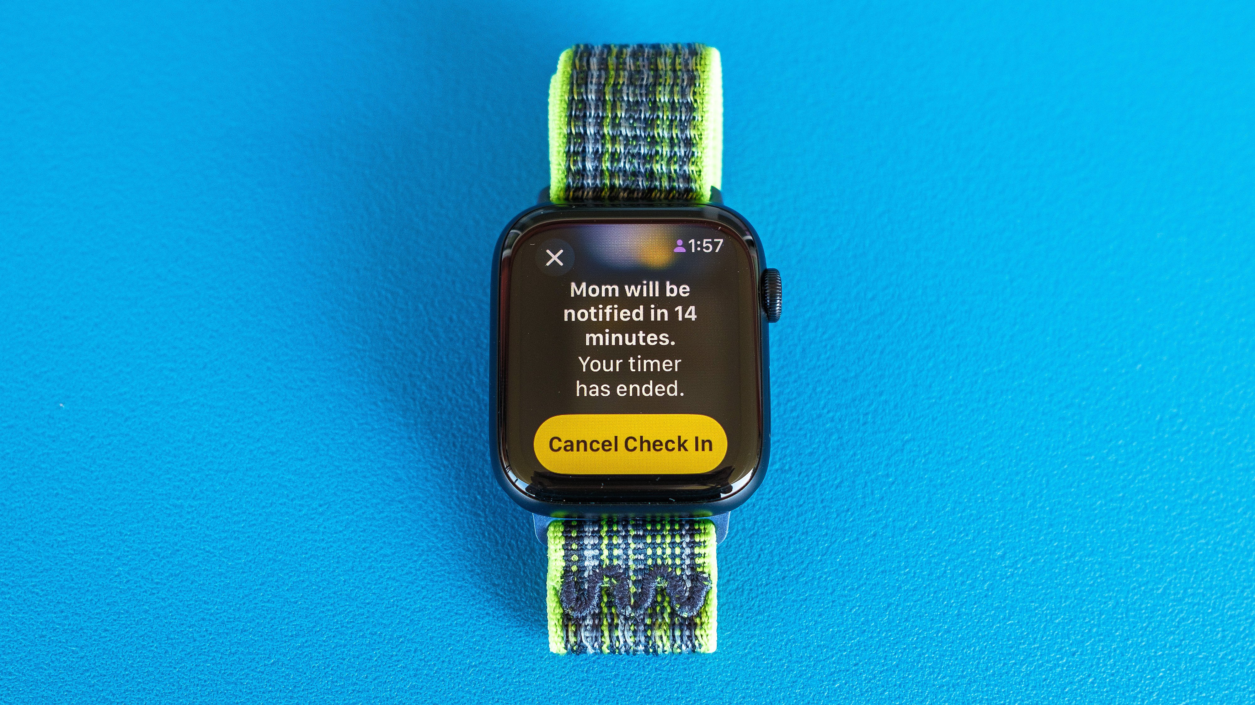 A detailed shot of Apple Watch SE against a light blue background showing how to set up and send check-in notifications in watchOS 11. 