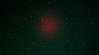 A faint red blob of light in the night sky