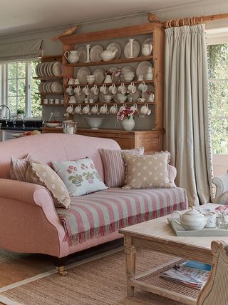 cottage living room with pink sofa, dresser with cups display
