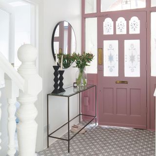 Hallway area with a pink front door, tiled floor, and white walls with a console table