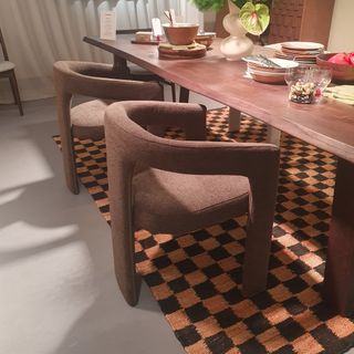 A dining room set-up from the John Lewis spring/summer 2025 press showcase with a dark wood dining table and a chequered jute rug