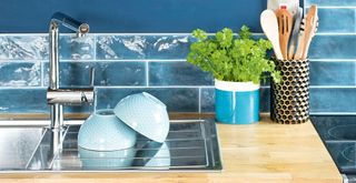 Blue kitchen with stainless steel sink and draining board with blue bowls drying and herb plant pot to one side