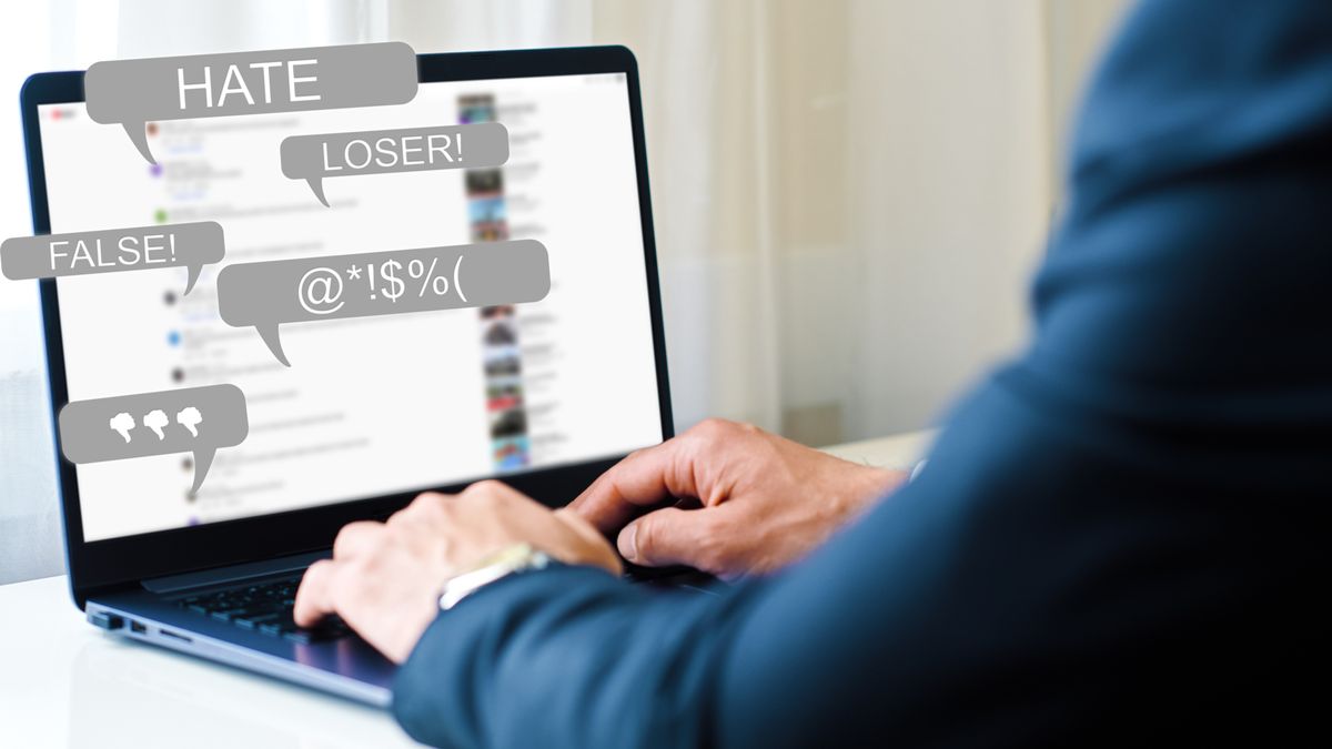 A man working at a laptop which displays messages of abusive nature