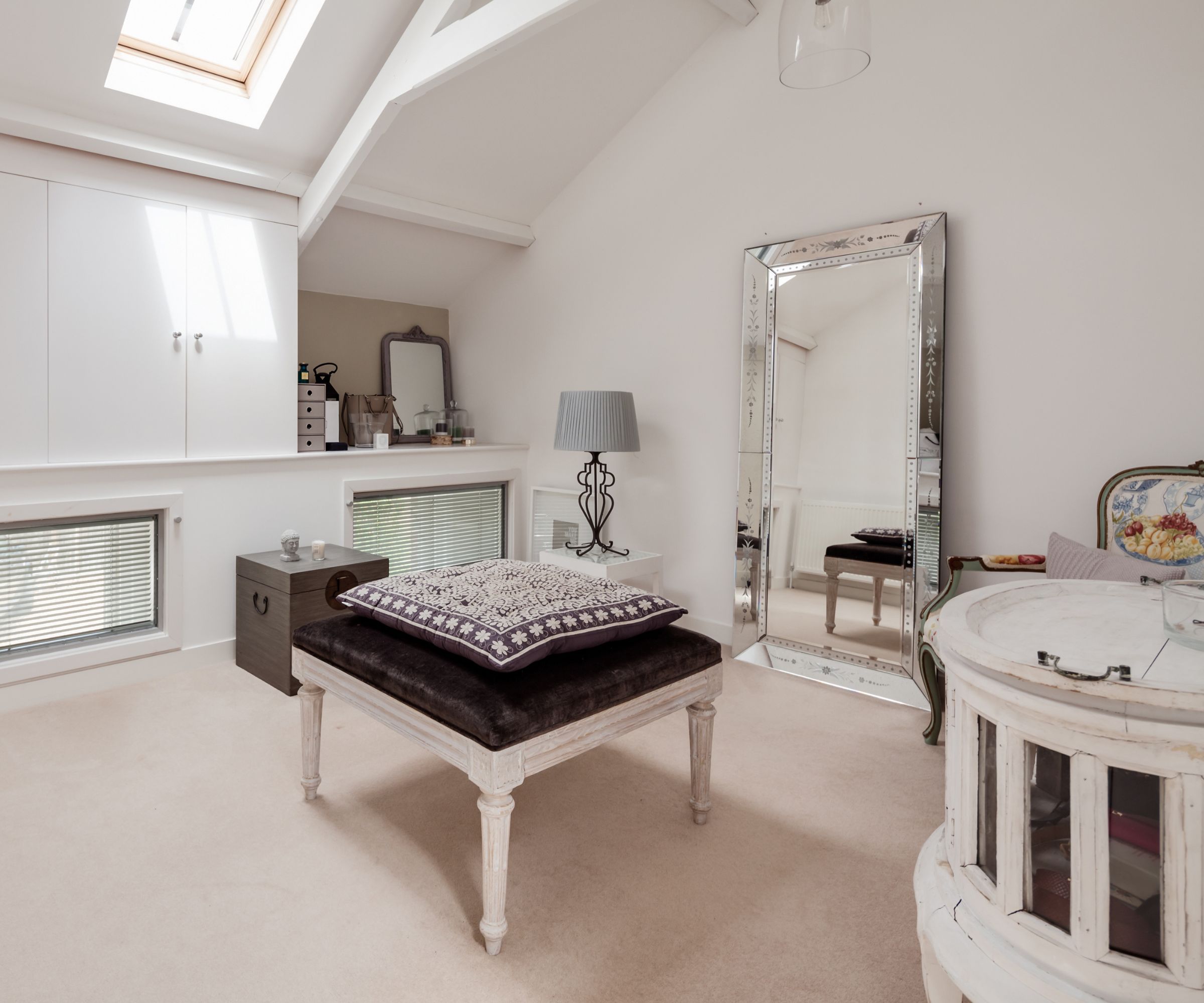 Bright sunlit luxury chic dressing area simply decorated in shades of white with built in cupboards, stool and mirror