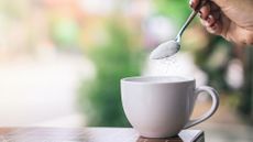 A woman spoons a sugar substitute into a mug. 