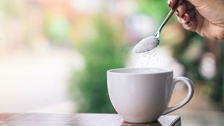 A woman spoons a sugar substitute into a mug. 