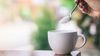 A woman spoons a sugar substitute into a mug.
