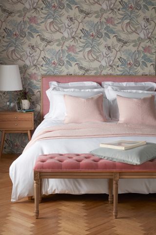 A pink velvet bed with white linen and floral wallpaper