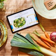 Tablet with recipe on a wooden surface with leeks and carrots