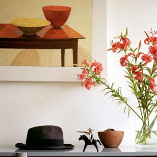 A dark grey hard, cowboy on a horse , brown bowl and vased flower on a grey surface with a wall art above on a wall