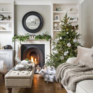 decorated Christmas tree in neutral living room with round mirror above fireplace