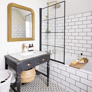 antique console table sink unit, with a white metro tiled bath and shower area and gold framed mirror