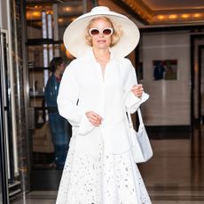 Pamela Anderson wearing a white outfit with a sun hat, button up shirt and white sunglasses