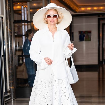 Pamela Anderson wearing a white outfit with a sun hat, button up shirt and white sunglasses