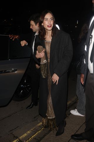 Alexa Chung wearing a gold mesh dress with black tights to the British Vogue and Tiffany & Co. party during London Fashion Week alongside Tom Sturridge.