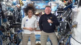 a man and a woman on the international space station, in a module full of wires, computers and other equipment