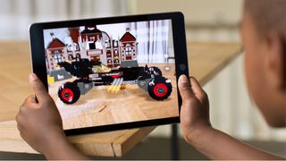 A man holds a tablet in front of an empty table, and sees a toy car through its AR app