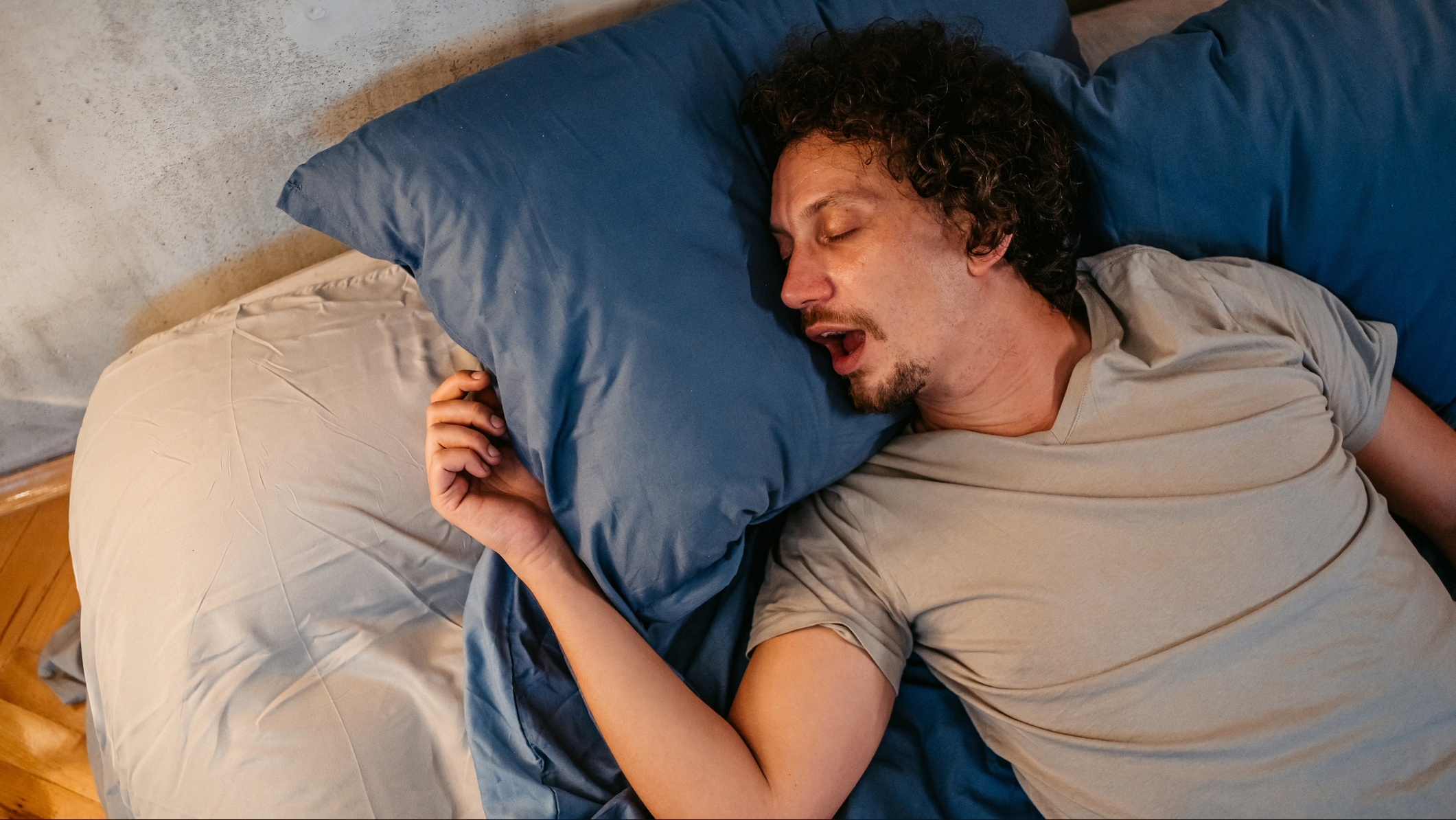 Man lying on his back in bed with his mouth wide open snoring