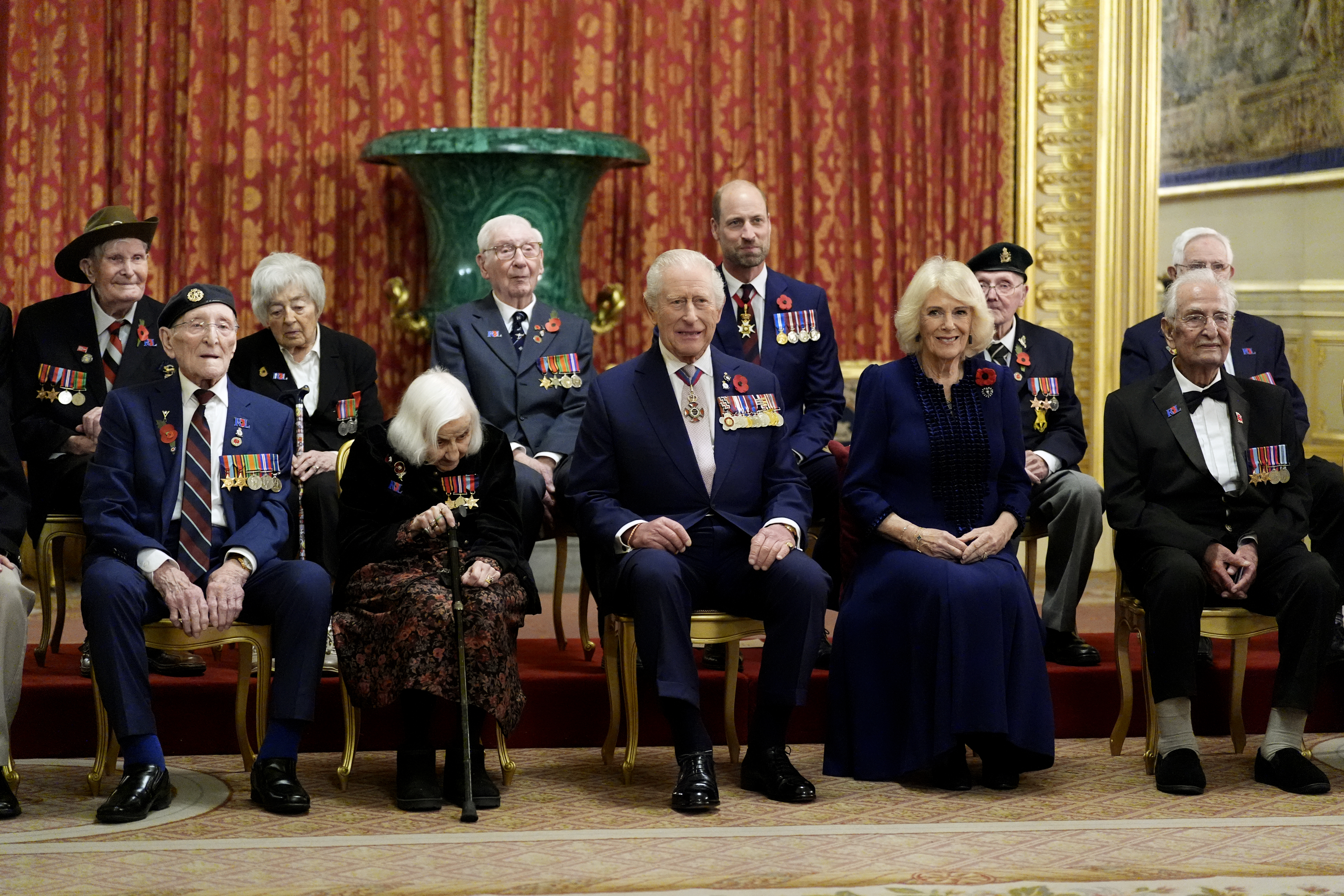 King Charles and Queen Camilla sitting in chairs with veterans and Prince William