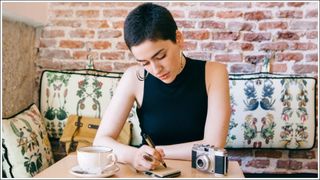 Young Woman With Short Hair Writing On Note Pad In Cafe