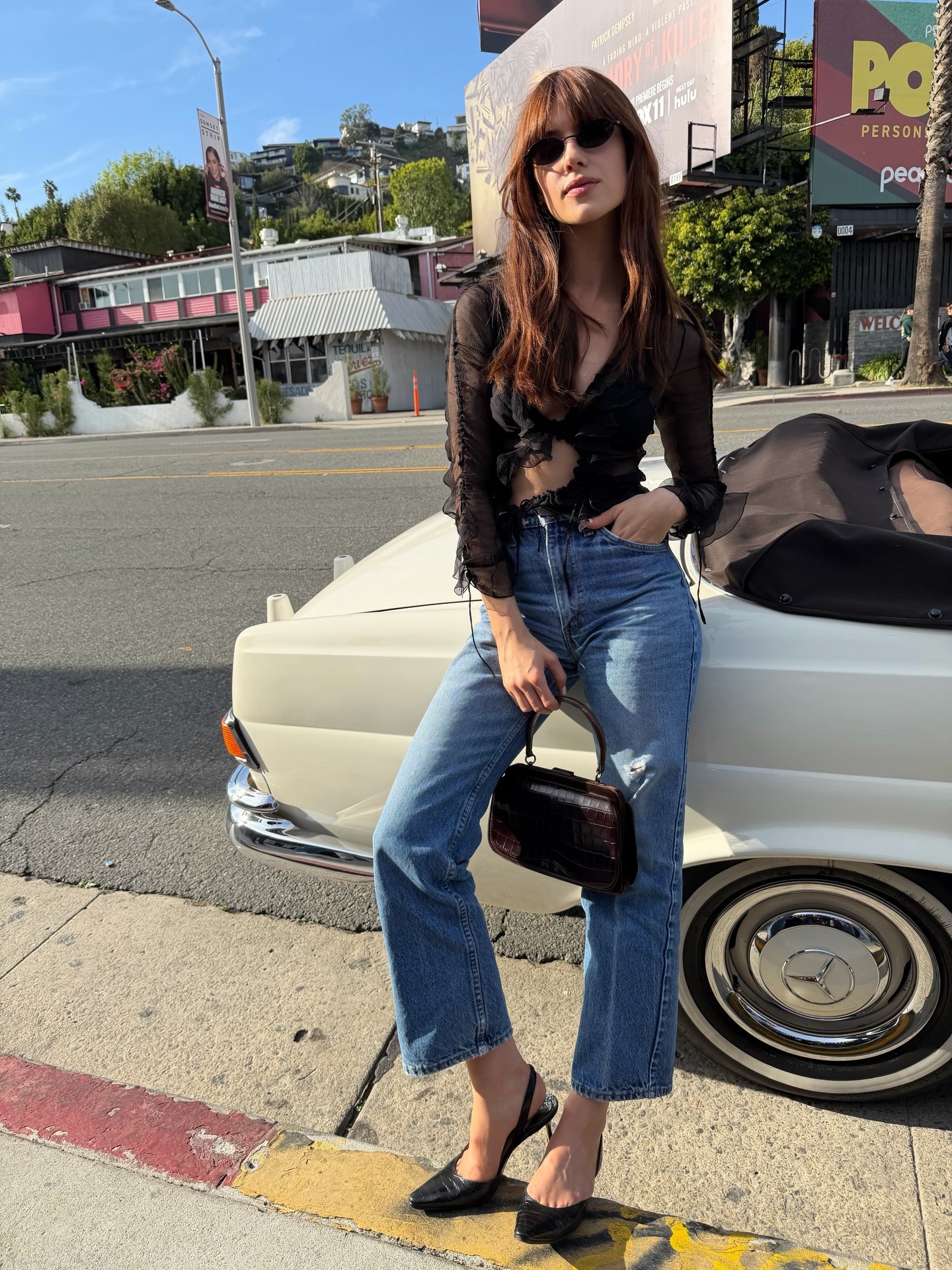 Daisy Edgar-Jones wearing a black going-out top with high-waisted jeans and a black vintage clasp bag on Sunset Boulevard in Los Angeles.