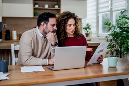 Couple at home managing personal finances, reviewing financial documents and monthly budget on a laptop, calculating bills