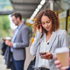 A young woman waits for the commuter train while on her mobile phone. 