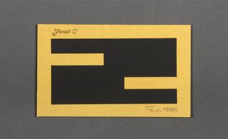 Front view of ﻿Fendi's black and gold invitation pictured against a grey background