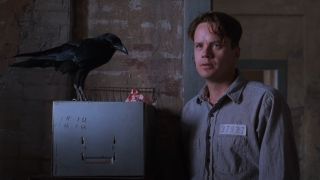 Tim Robbins stands next to Jake the crow standing on a filing cabinet in The Shawshank Redemption.