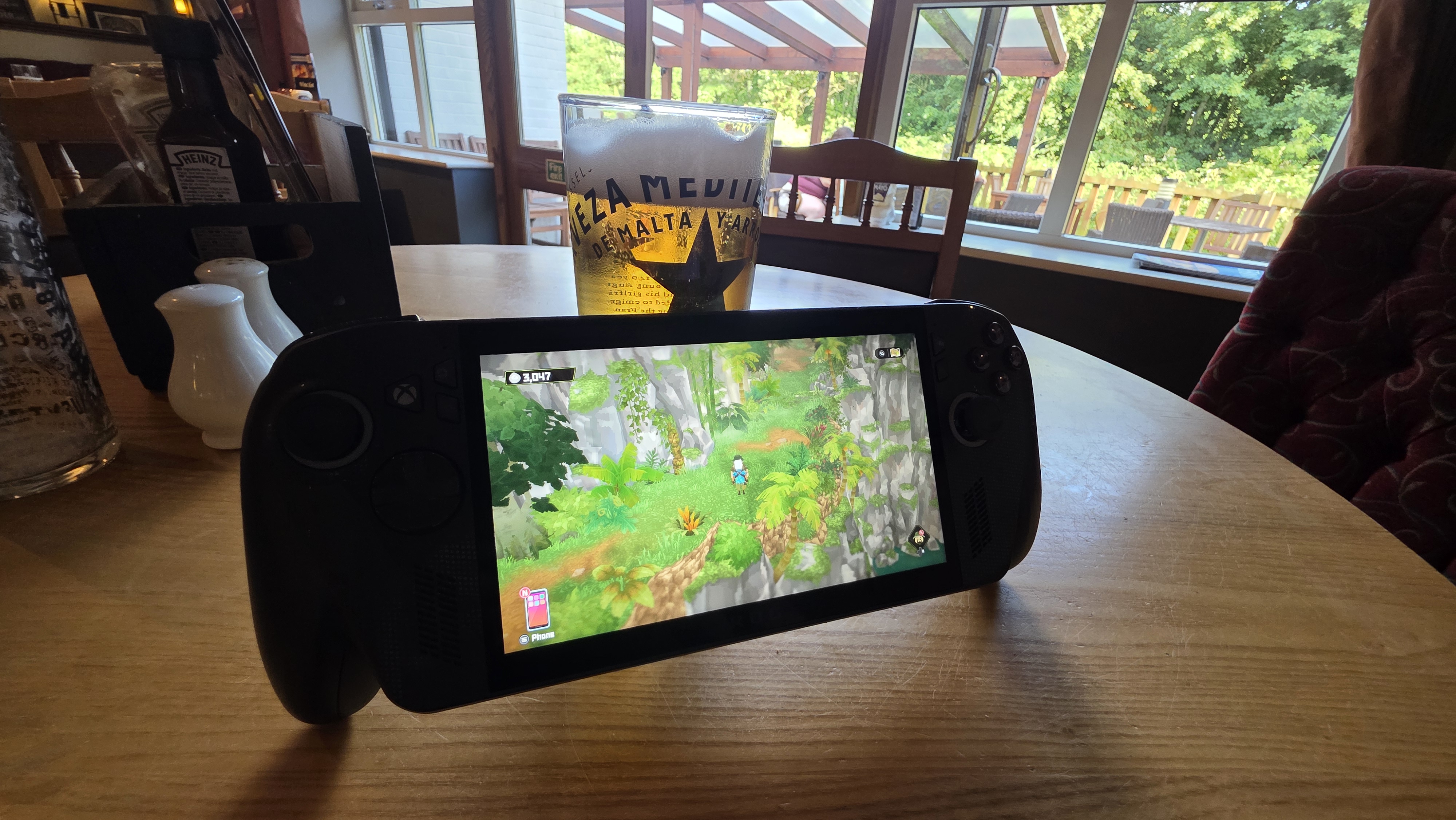 An Xbox Rog Ally X gaming console on a table, a pint of lager sits behind it.