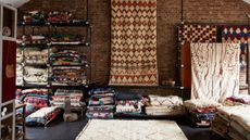 Showroom with shelves of folded rugs and a selection of rugs hung on the far wall and on the floor.