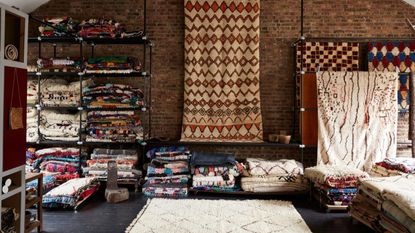 Showroom with shelves of folded rugs and a selection of rugs hung on the far wall and on the floor.