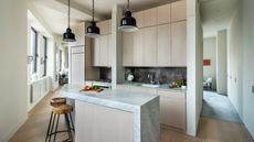 A tiny modern one-wall kitchen with an angular shaped island, slab cabinets, and three pendant lights overhead