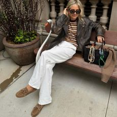 Blonde woman sitting on bench wearing white trousers, a striped top and suede loafers.
