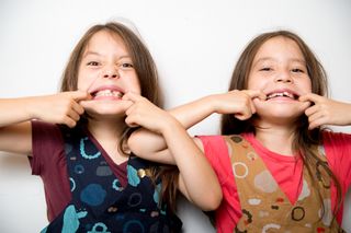 Two young female twins pulling a funny face with their fingers in their mouth