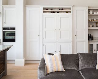 A gray sofa in front of white, built-in floor to ceiling cupboards