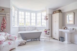 bathroom with white painted floor chintz chair freestanding tub and bay window