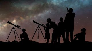 A group of people look up at the night sky through telescopes.