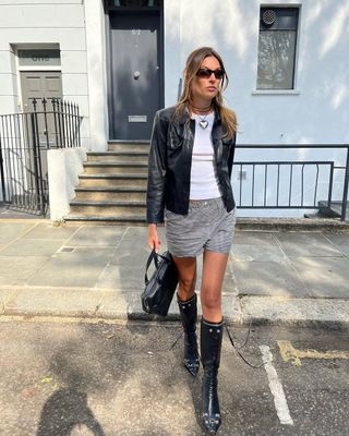 Woman wearing boxer shorts, leather jacket, and tall black boots.