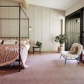 bedroom with white panelling and pink carpet, a four poster bed coverd in white bedlinen and a thick gauge knitted throw