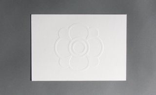 Front view of ﻿Emanuel Ungaro's white embossed invitation pictured against a grey background