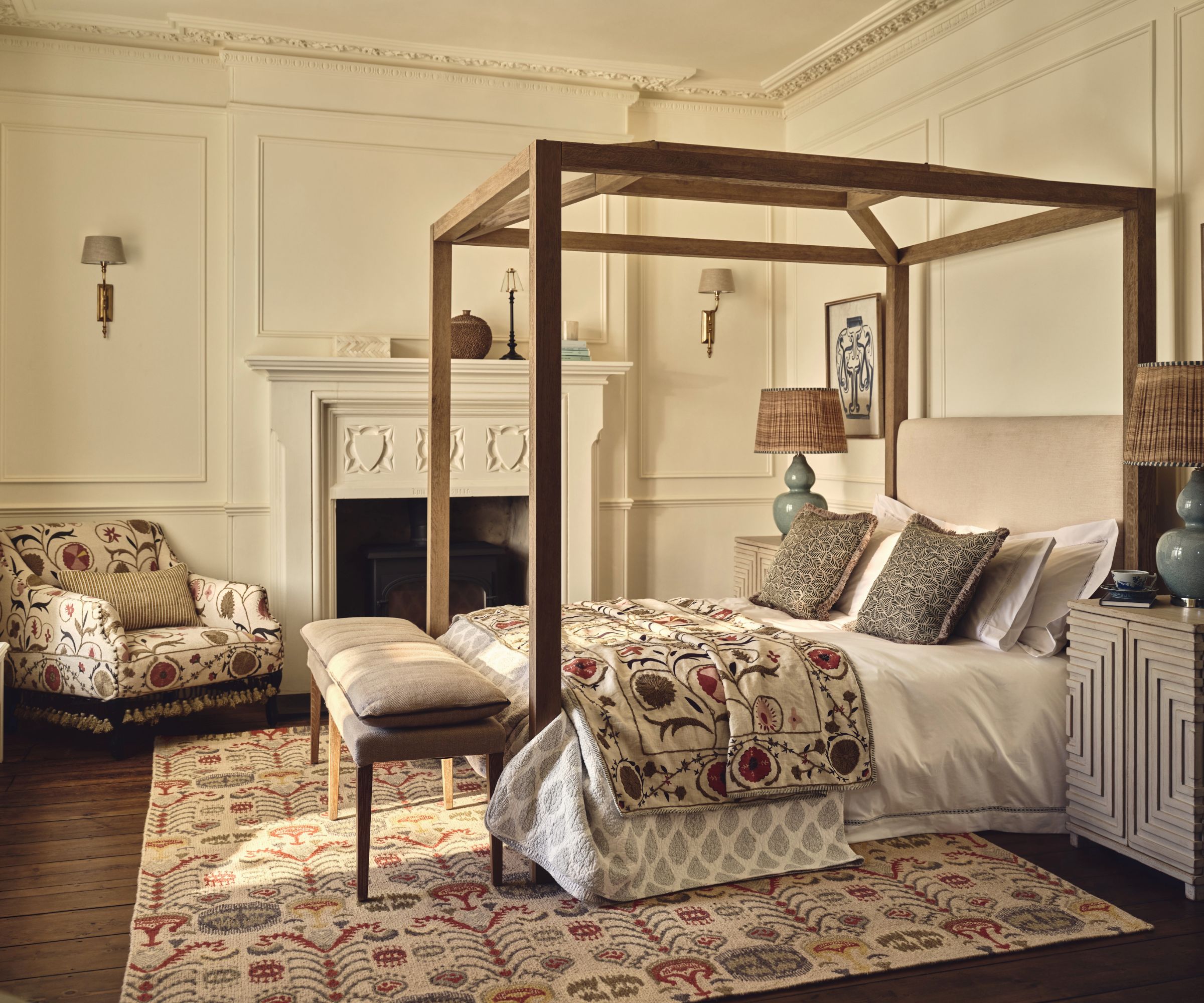 Traditional bedroom with a wooden four-poster bed acting as a subtle room divider, patterned textiles, fireplace and soft neutral walls.