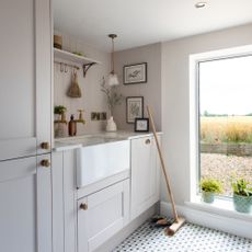 Beige painted utility room with a sink and a broom leaning against the cabinets