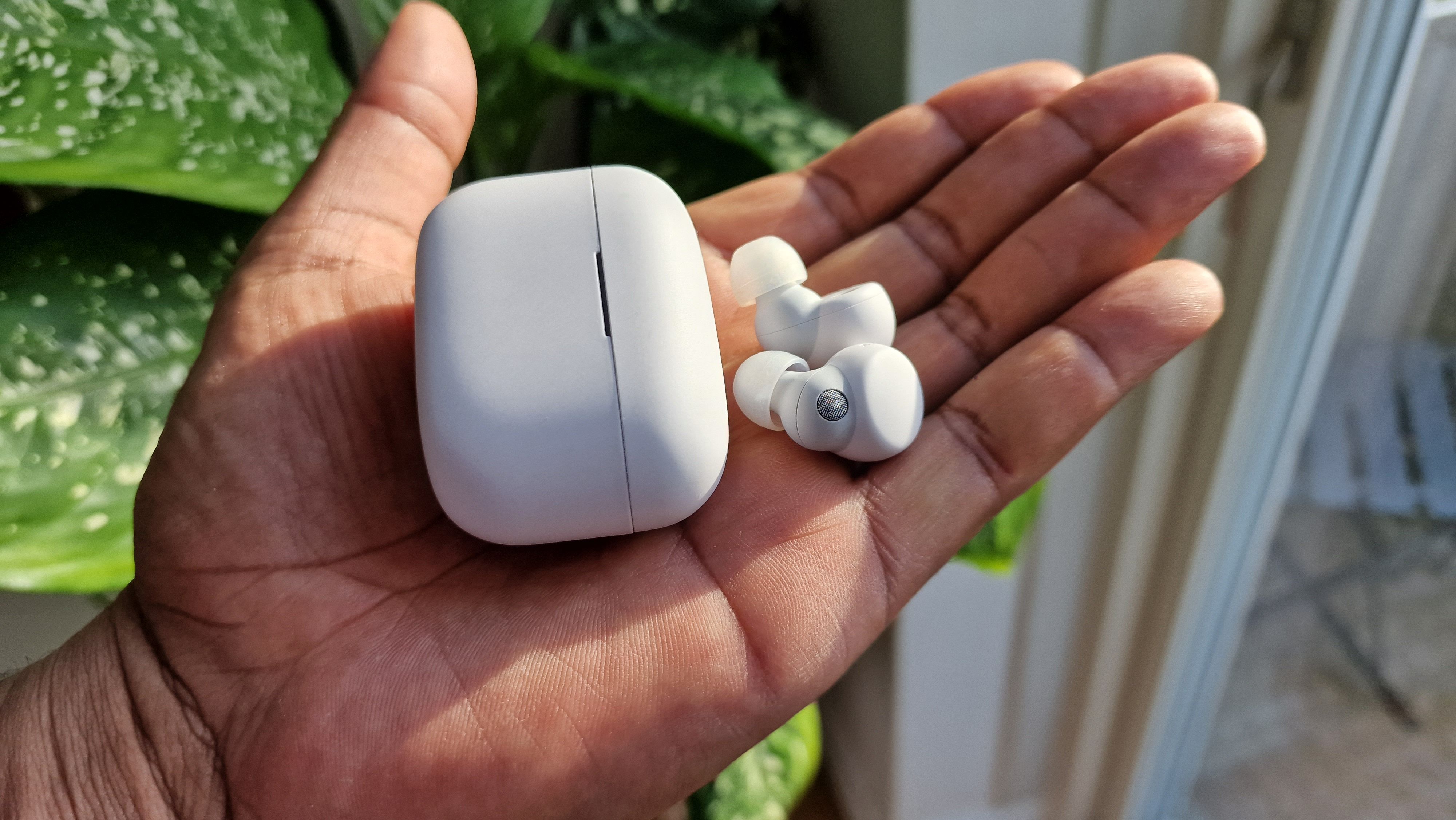 Sony Linkbuds S ligger på en håndflade sammen med deres etui.